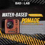 Bad Lab Water-Based Pomade Jet Black container shown on a dark promotional graphic with yellow hazard stripes and text highlighting strong hold and water-based formula.