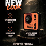 A tin of BAD LAB Jet Black Water Based Pomade displayed on stacked dark stone blocks, with dramatic lighting and a dark textured background. Text on the image highlights 'NEW LOOK', 'WINDPROOF HOLD', 'STRONGER HAIR*', and 'IMPROVED FORMULA'.