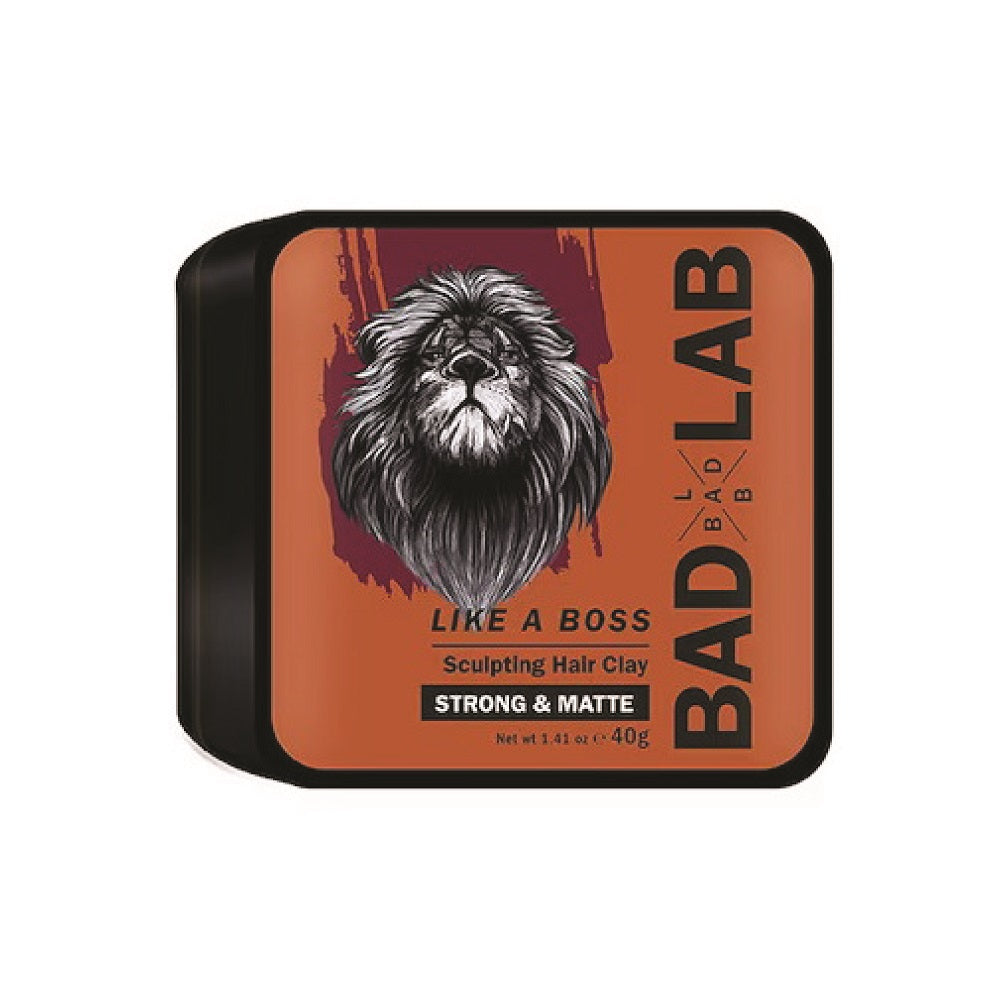 A rectangular tin of Bad Lab Like A Boss Sculpting Hair Clay in Strong & Matte, featuring a black lid with a prominent lion graphic on an orange background.